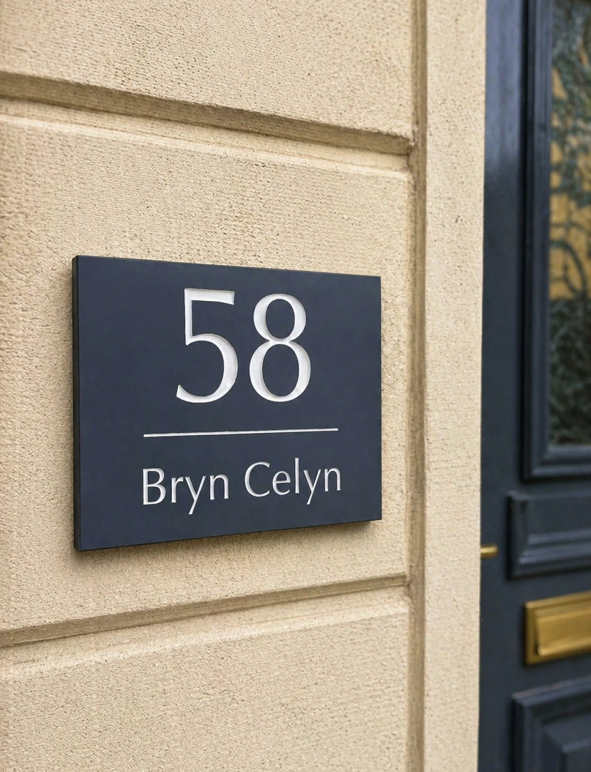 A dark navy blue rectangular house number plaque mounted on a beige textured wall, next to a dark blue door. The plaque features the number 58 in large white font, with the name Bryn Celyn in white serif text below.