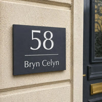 House number sign '58 Bryn Celyn' on a brick wall next to a door.
