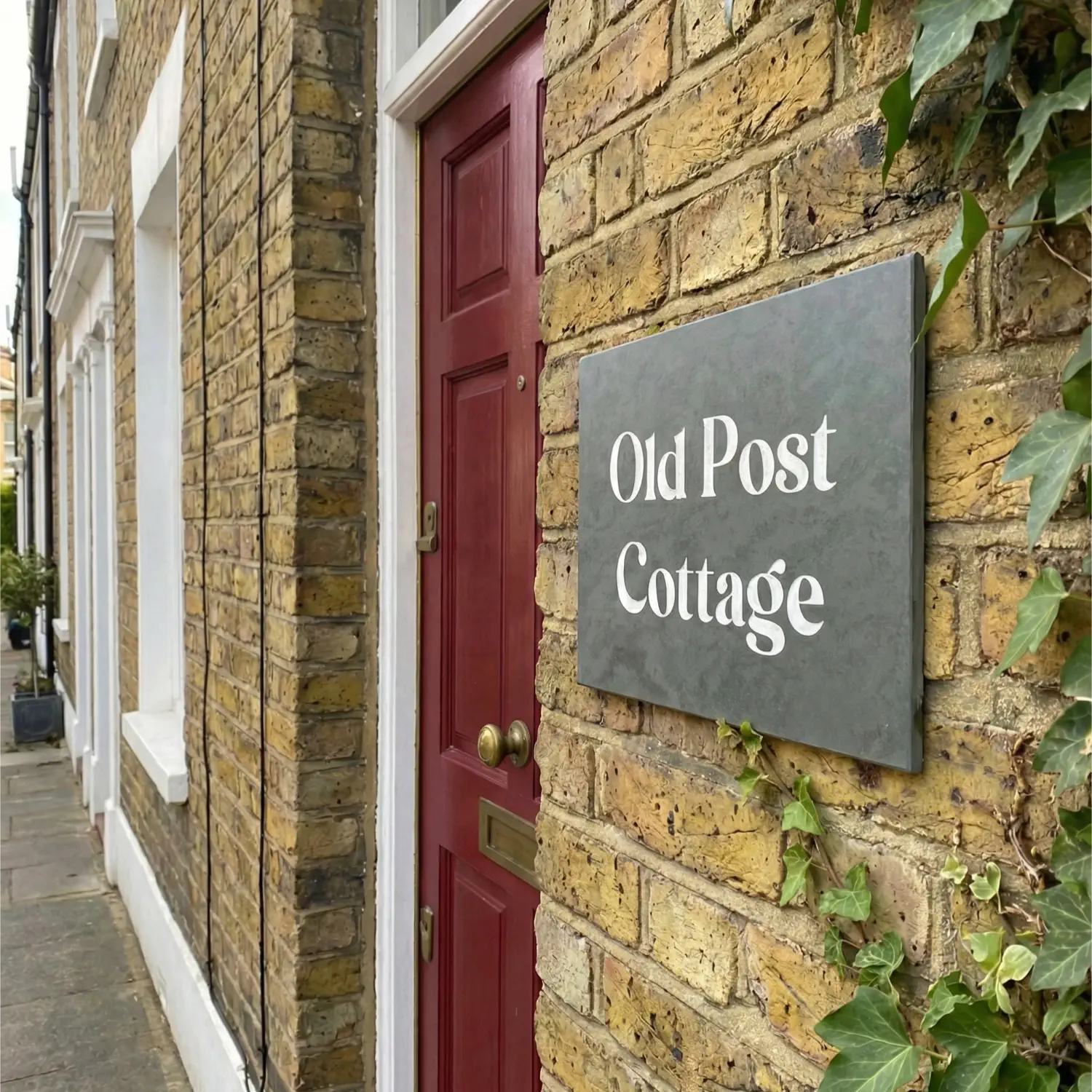 a grey slate house sign on a red brick wall reading The Weald.