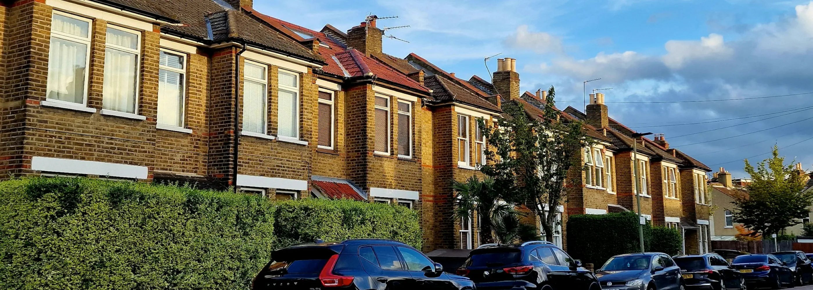 Row of residential houses with cars parked along a street on a clear day.
