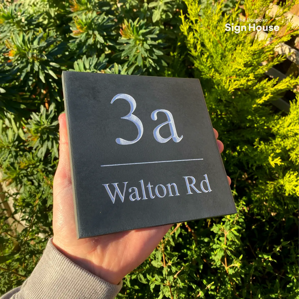 a simple slate house sign with the house number and street name engraved into the surface and painted white. the font is times new roman