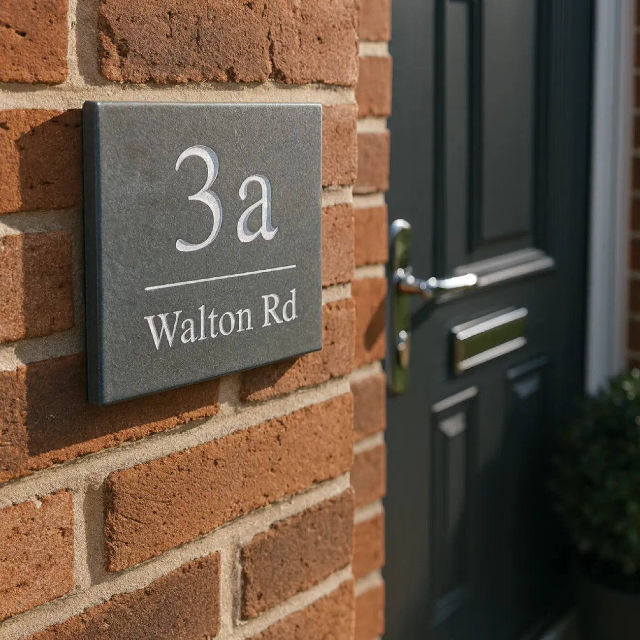 a simple slate house sign with the house number and street name engraved into the surface and painted white. the font is times new roman
