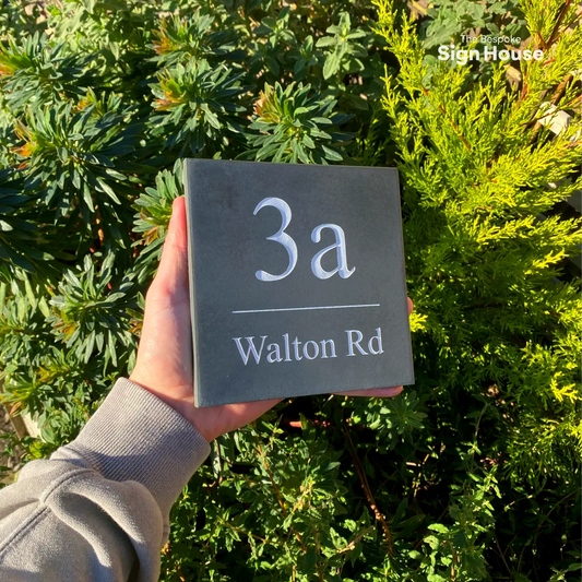 a simple slate house sign with the house number and street name engraved into the surface and painted white