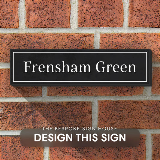 A granite house sign engraved with the word 'frensham green' displayed on brick wall of a house.