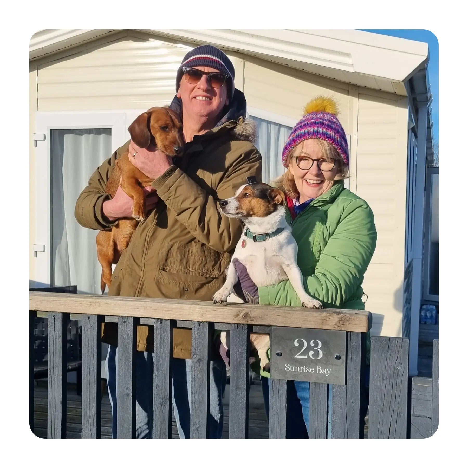 Two people with two dogs standing in front of a trailer with 'Sunrise Bay' on it.