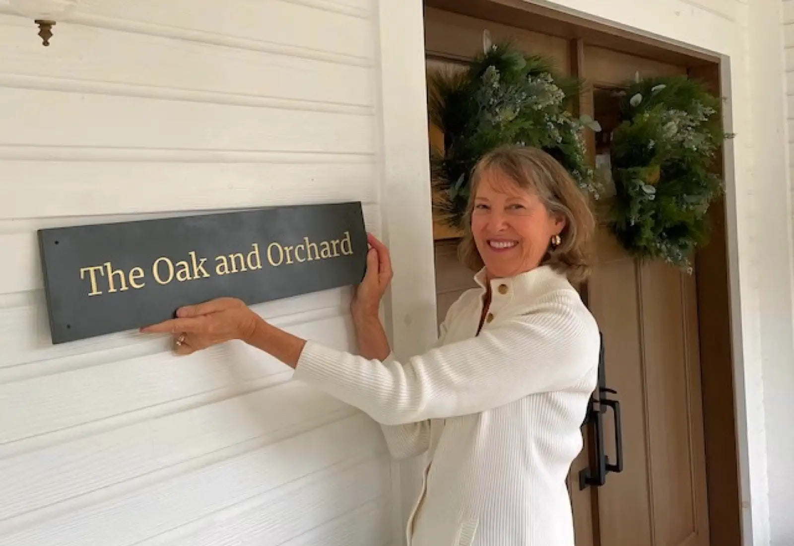Woman placing a sign on a garage door with wreaths in the background