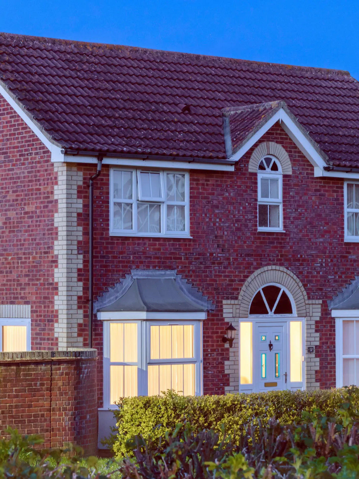 Red brick house with white windows and a blue door at dusk.