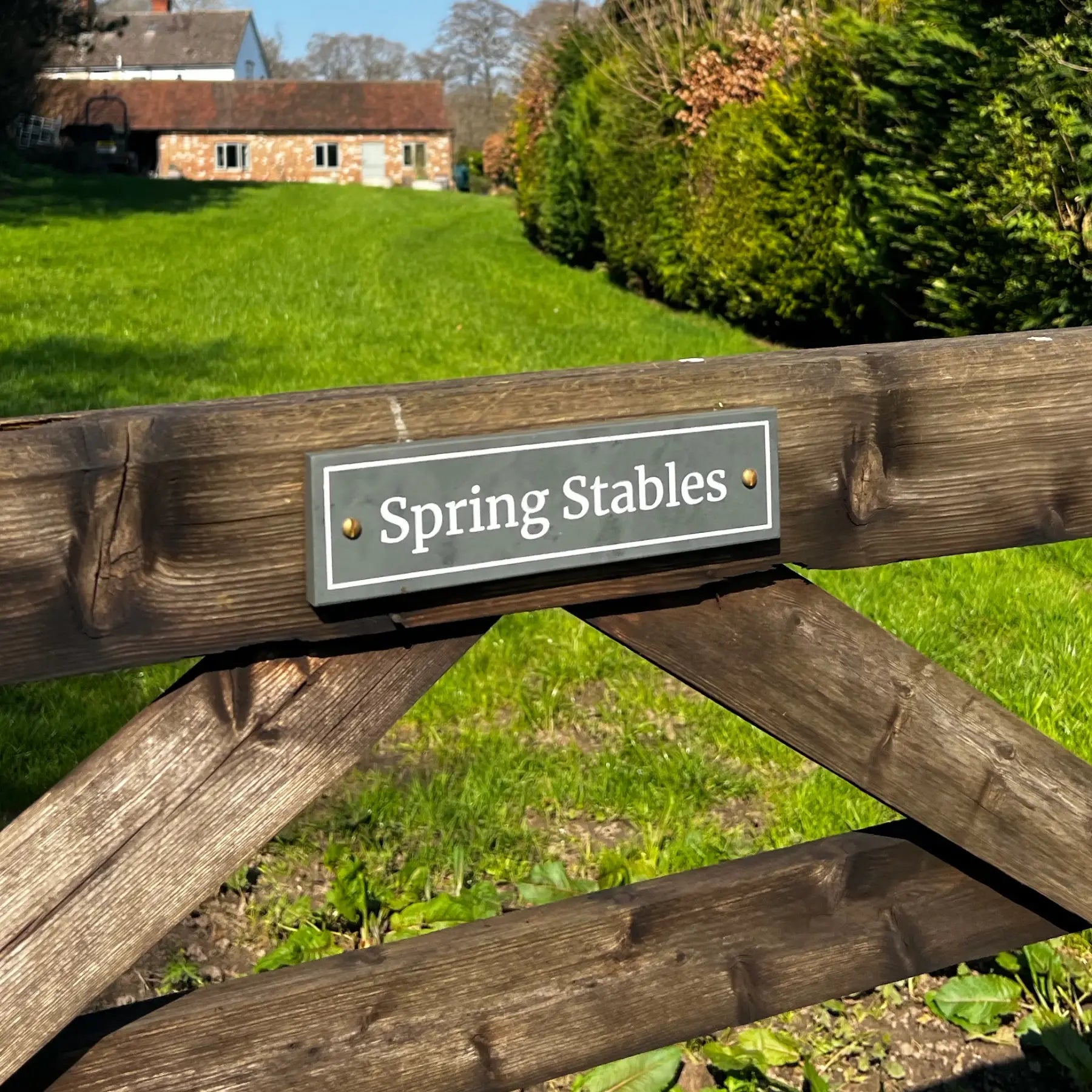 Wooden gate with 'Spring Stables' sign in a grassy area with a building in the background