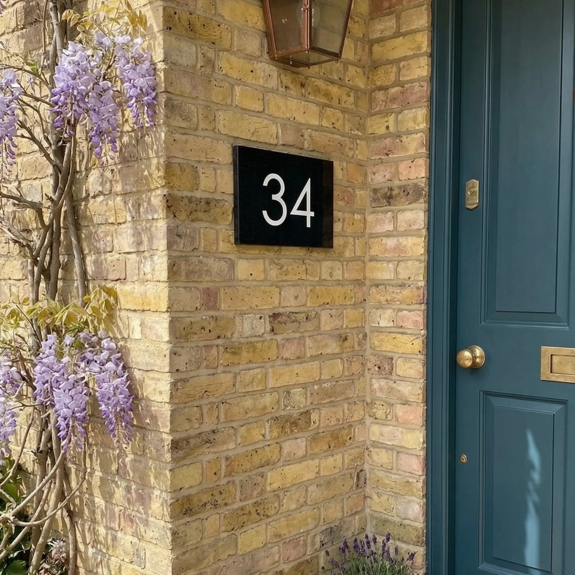 House number 34 on a brick wall with a blue door and wisteria plant.