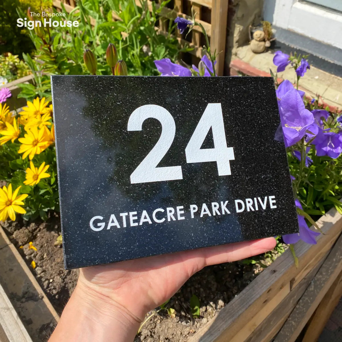 black granite sign with white galaxy effect amongst garden flowersGranite wide rectangle number and name sign.