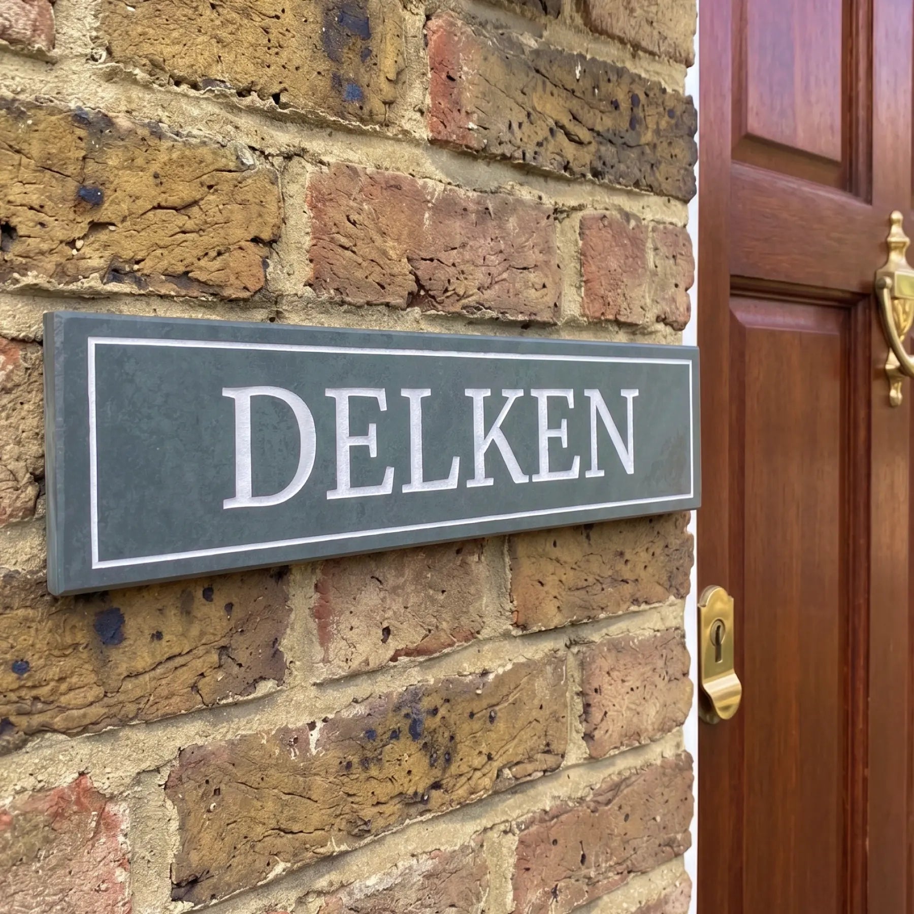House sign with 'DELKEN' on a brick wall next to a wooden door.