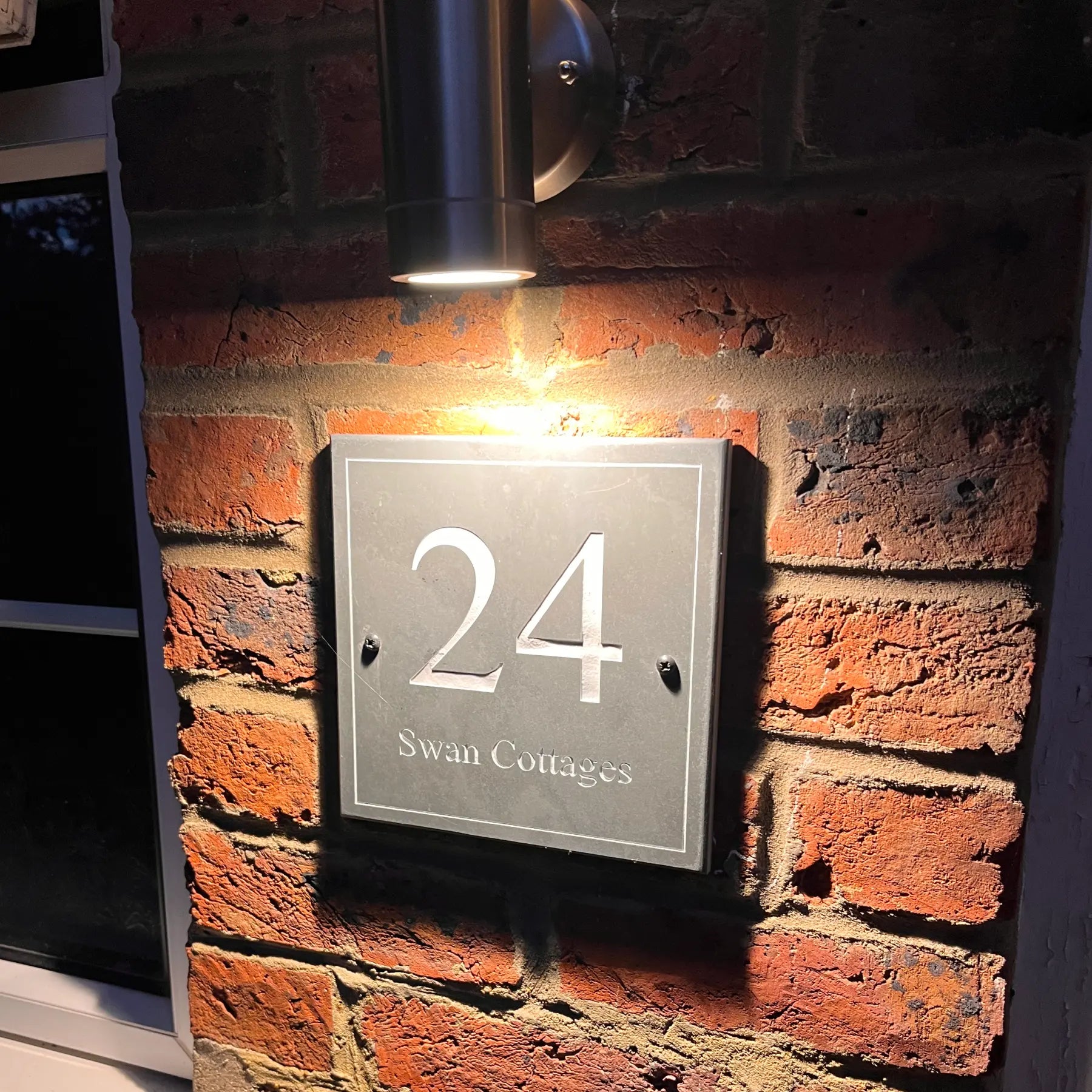House number 24 on a brick wall with a light fixture above