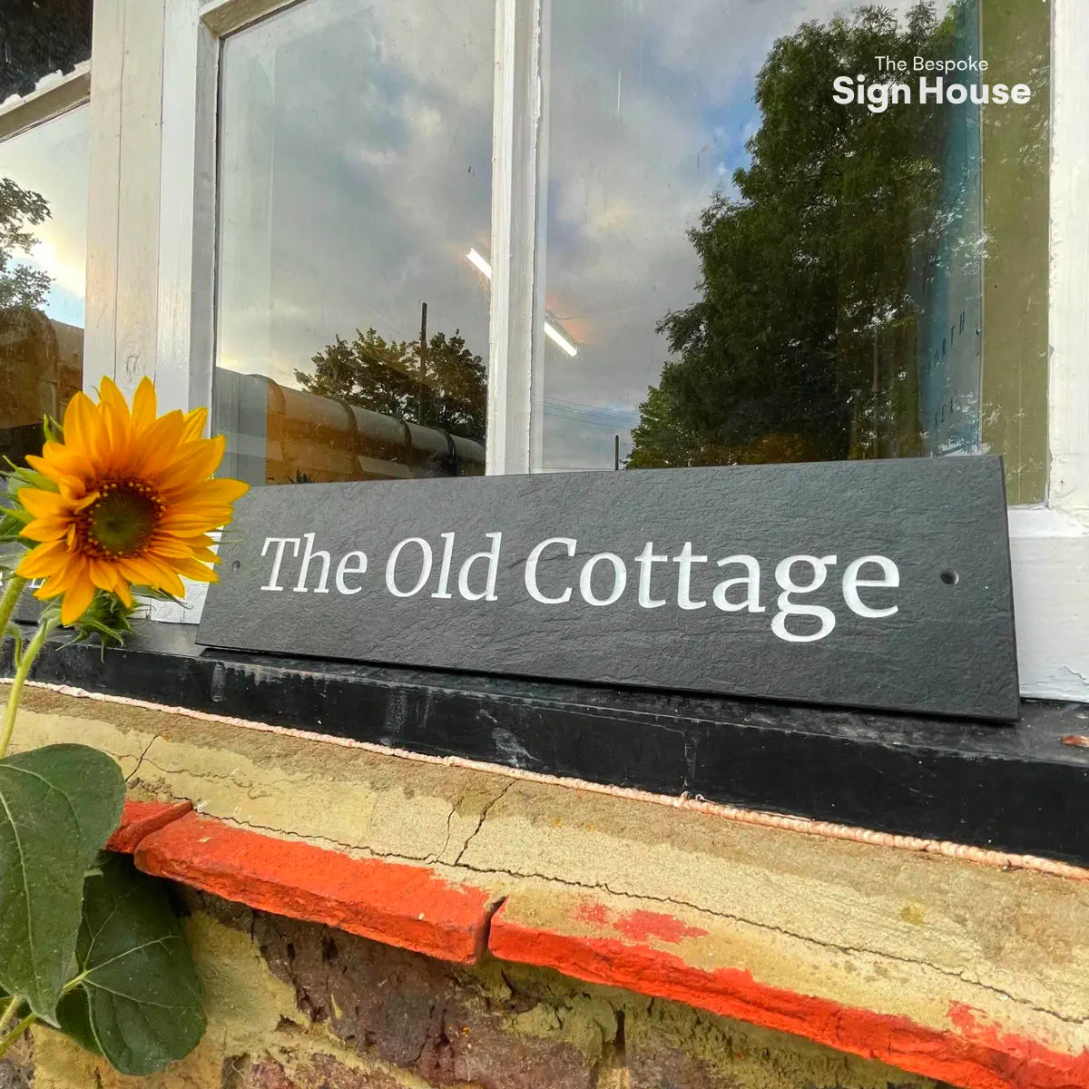 Long slate house sign on windowsill next to sunflower