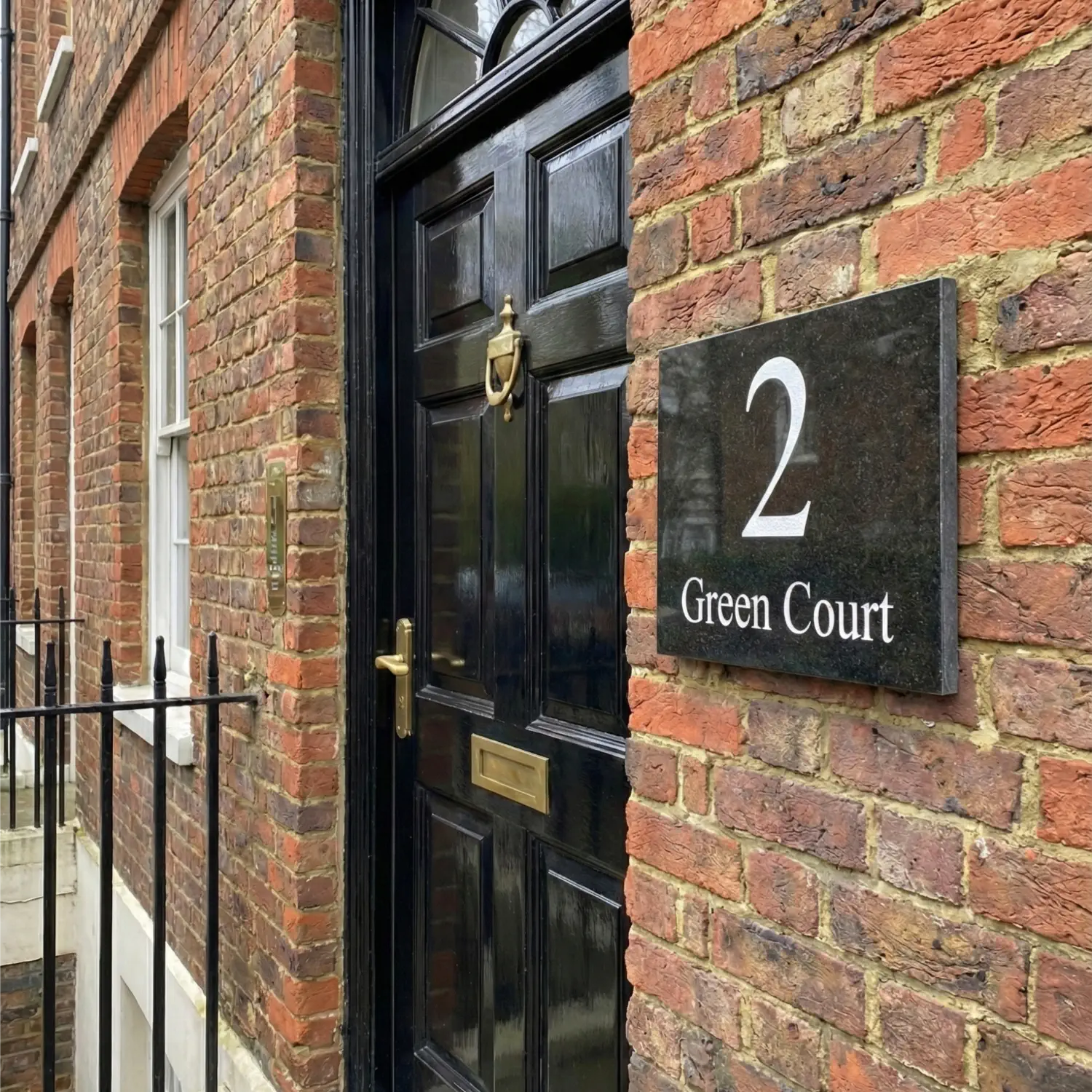 black granite house sign on brick wall next to black front door. sign reads 2 green court