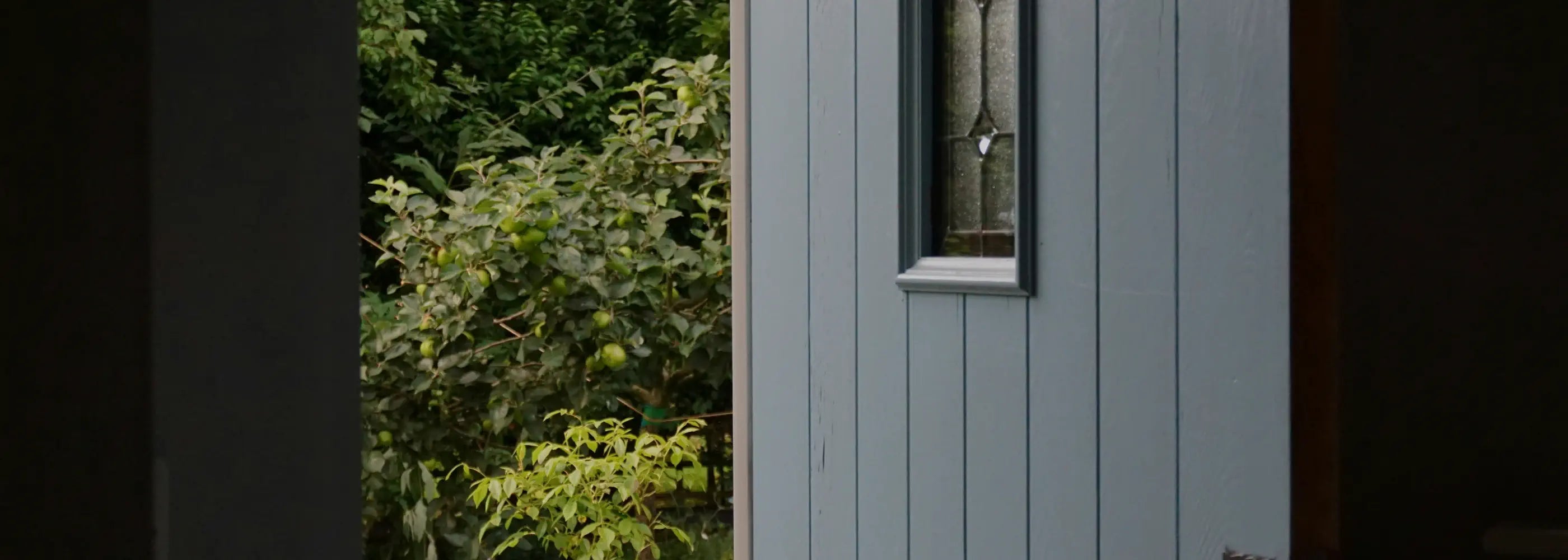 Light blue wooden shed with a window surrounded by greenery