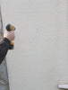 A video of a man installing a slate house sign on the front of his homes wall. He drillstwo holes in the wall with an electric drill, then installs the sign with screws using a screwdriver. At the end he gives a thumbs up to the camera.