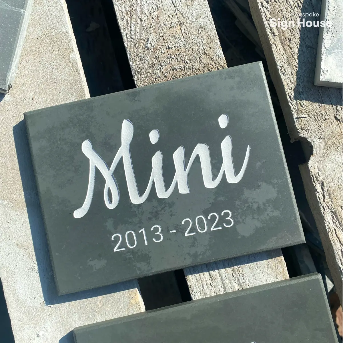 a rectangle slate memorial plaque with a pet name and dates engraved into it. The sign reads Mini 2013 to 2023