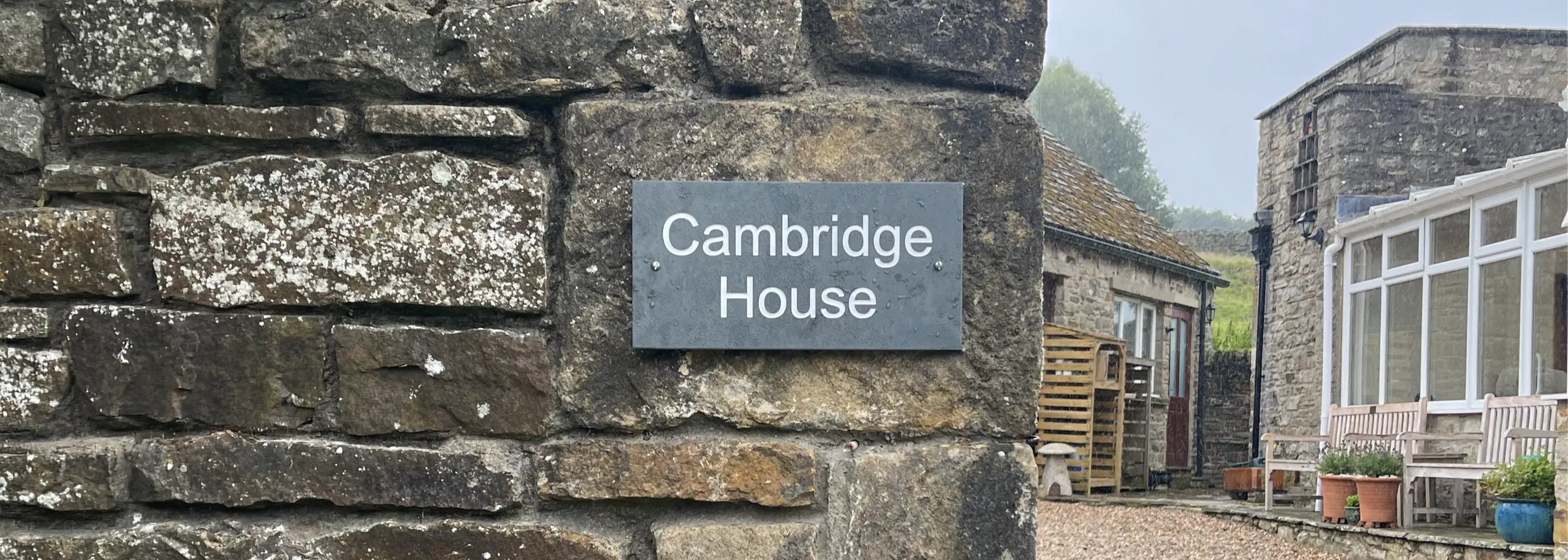Stone wall with a sign reading 'Cambridge House' in a garden setting.