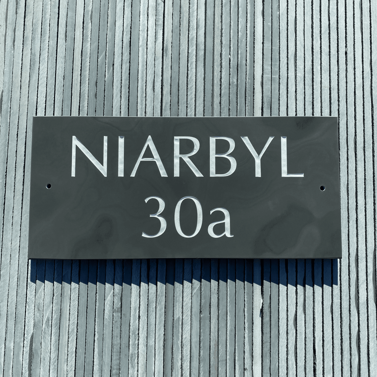 a simple grey slate house sign with bold lettering against a grey background