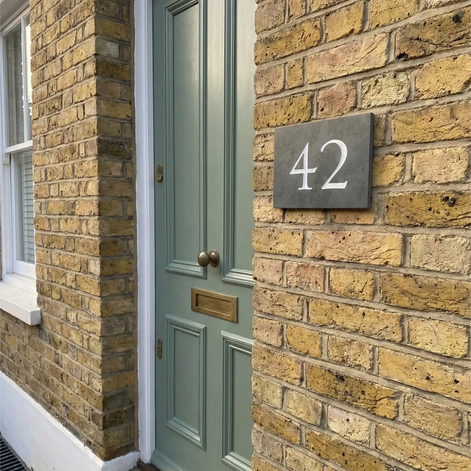 House number '42' on a brick wall next to a door with a plant in the foreground.