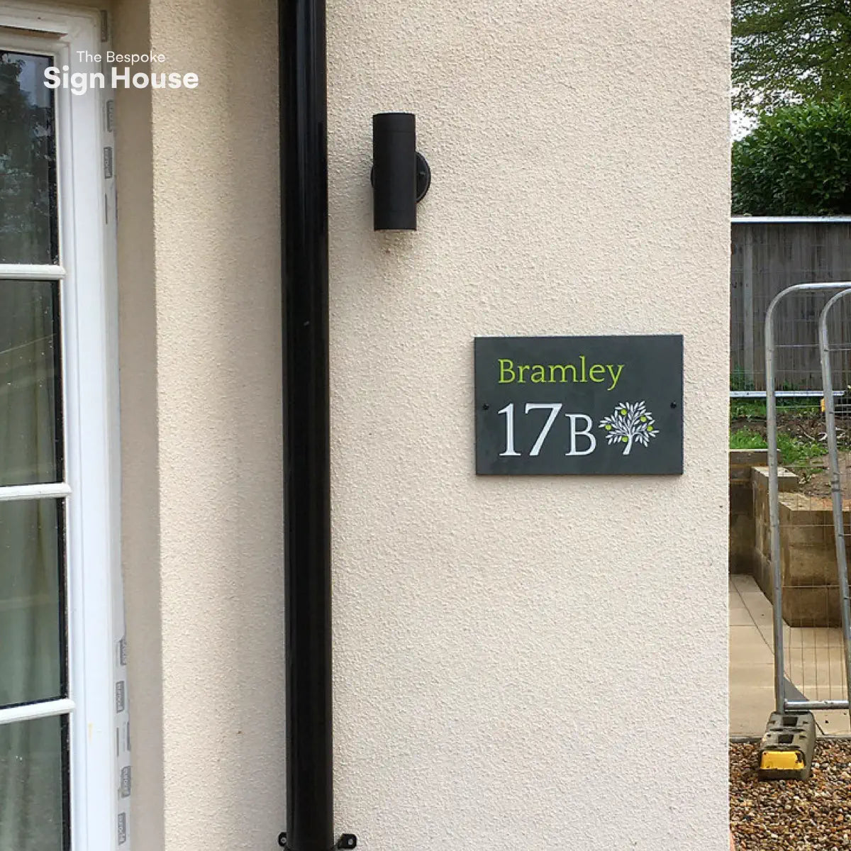 A slate house sign with green writing and an apple tree design displayed next to a front entrance of a home.