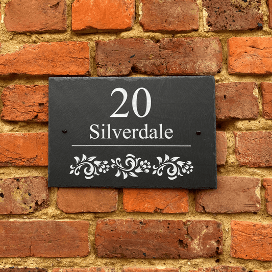 chiselled welsh slate sign with house number and road name above an intricate white floral design
