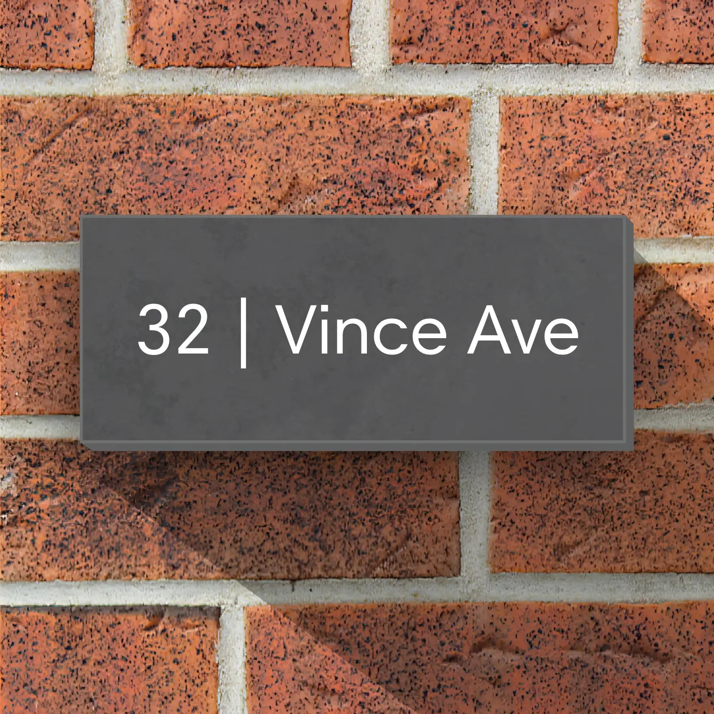 A modern grey slate house sign reading “32 | Vince Ave,” mounted on a red brick wall.