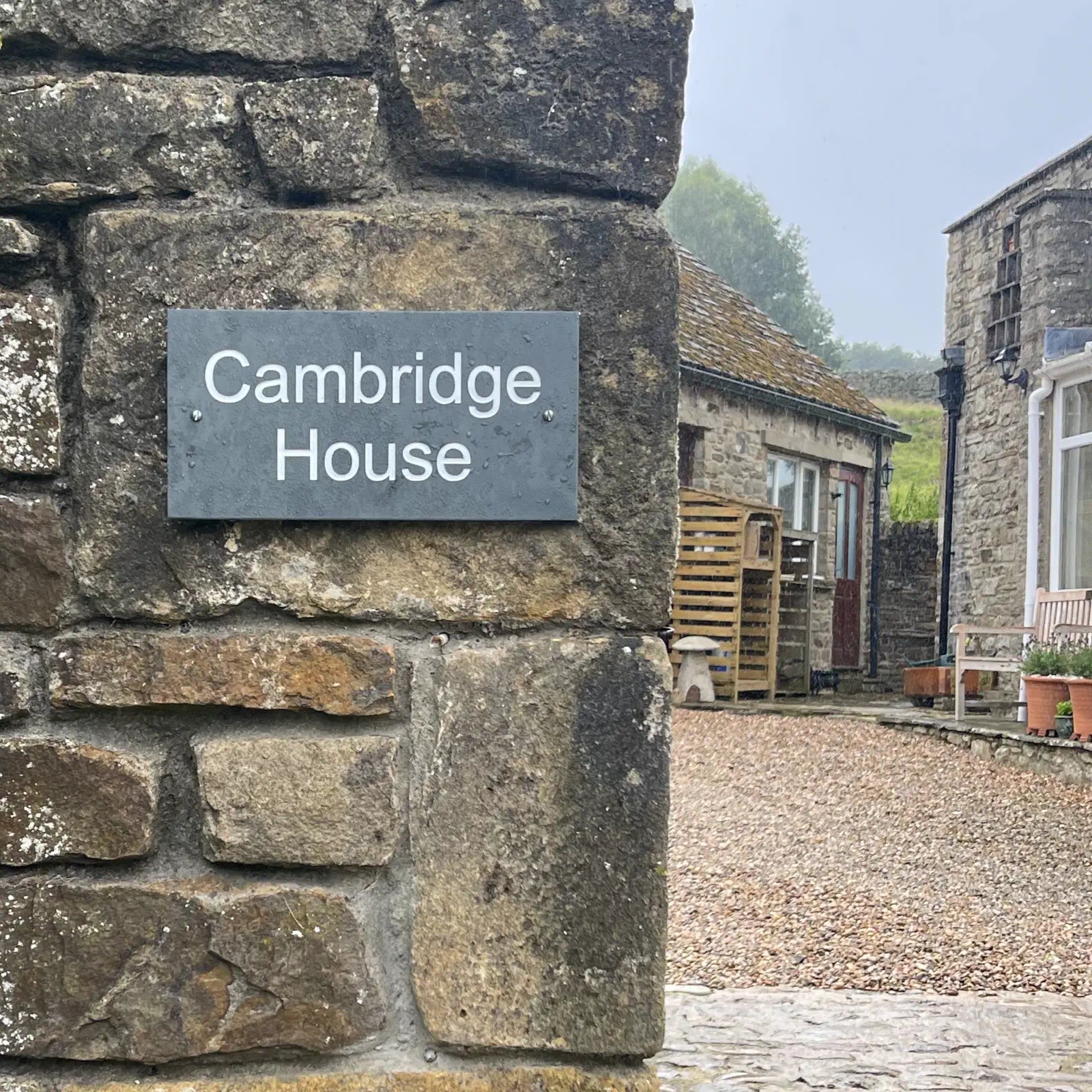 Stone wall with 'Cambridge House' sign and rustic building in the background