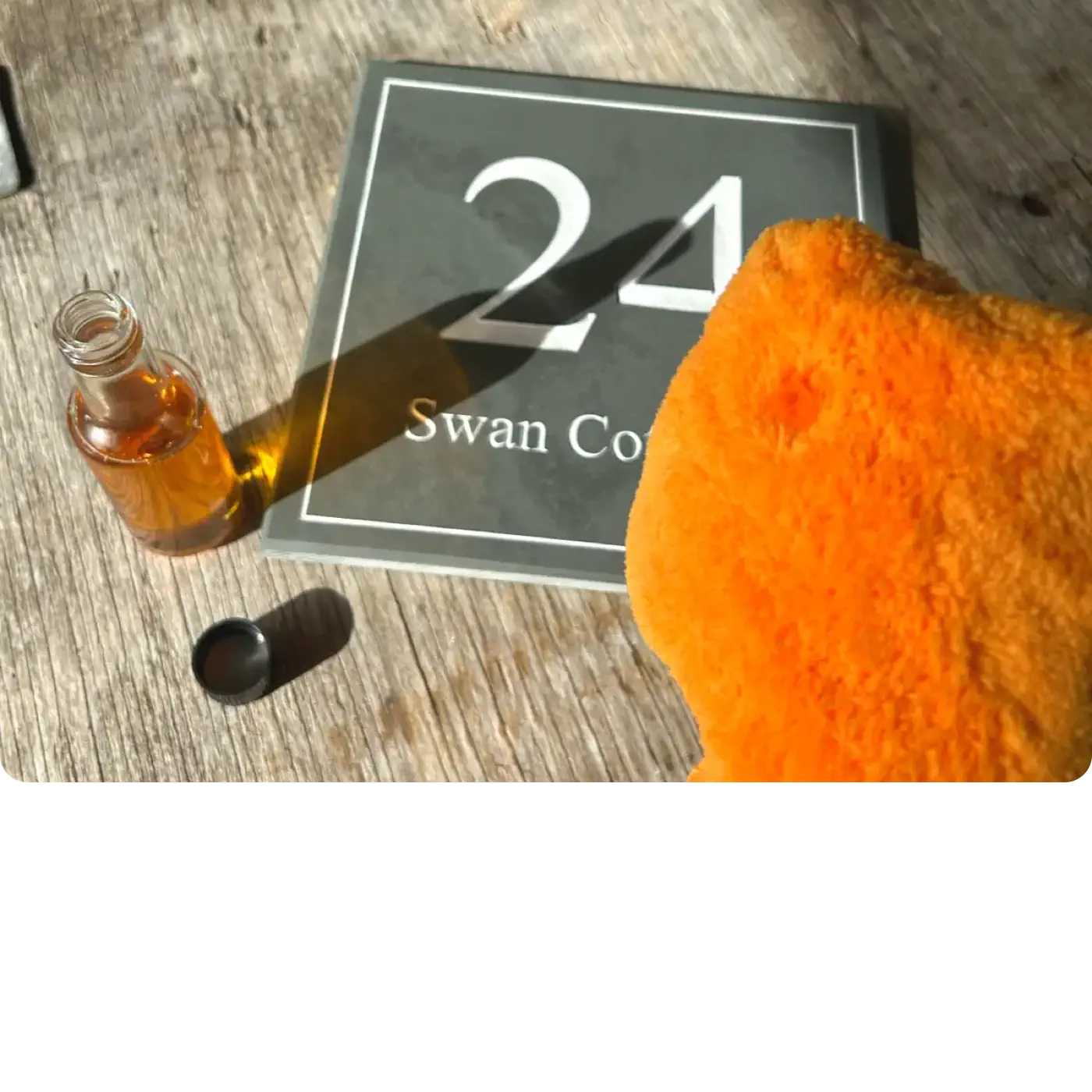 Orange bottle with black cap and orange towel on a light gray background