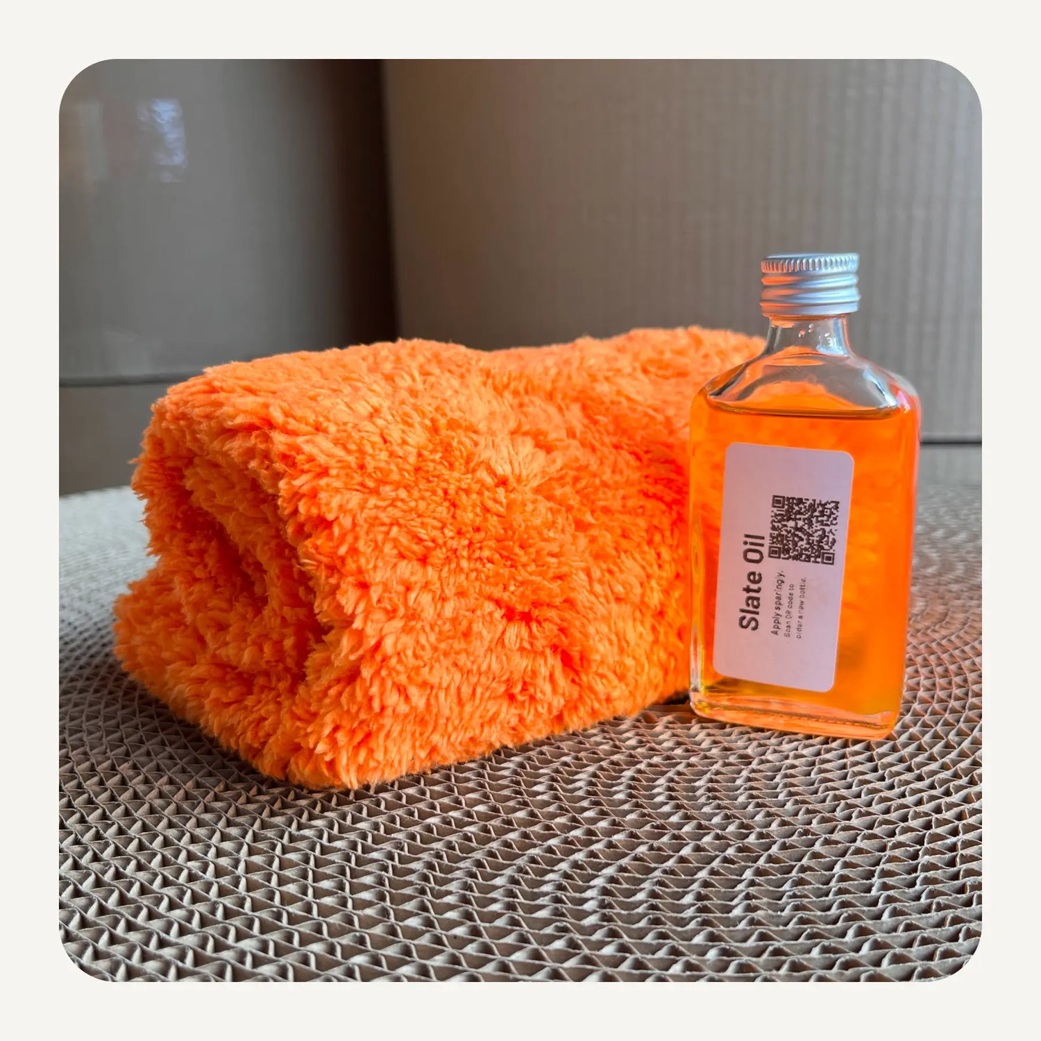 Orange towel on a wooden surface with a small bottle of liquid next to it.