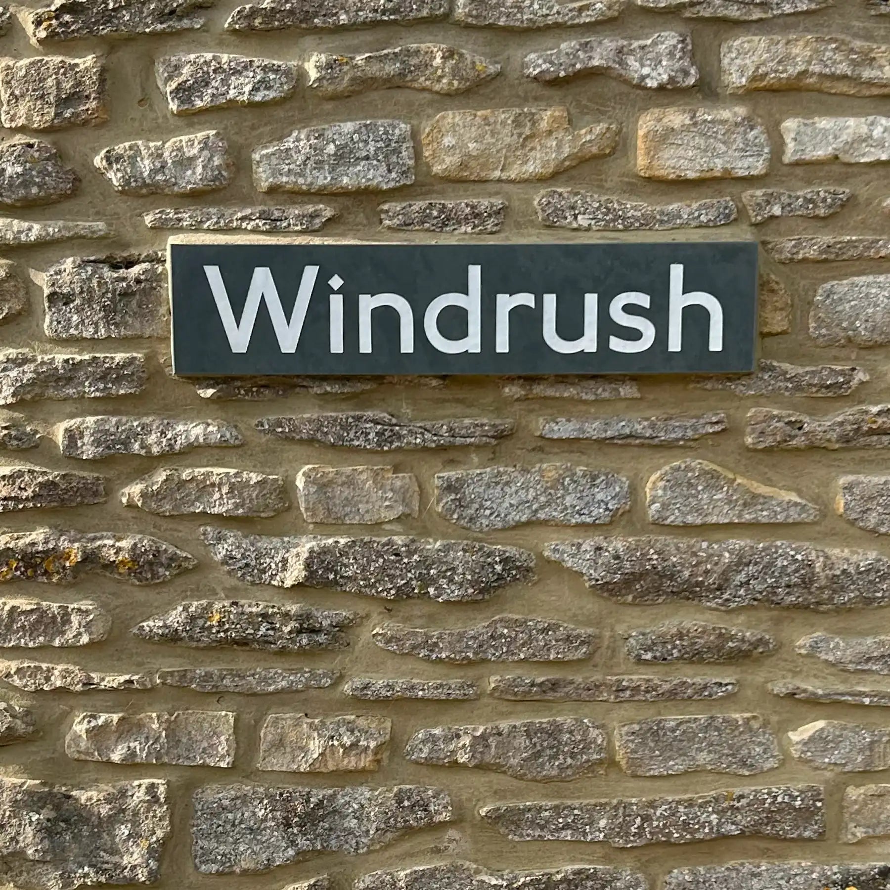 Slate sign with 'Windrush' text on a stone wall