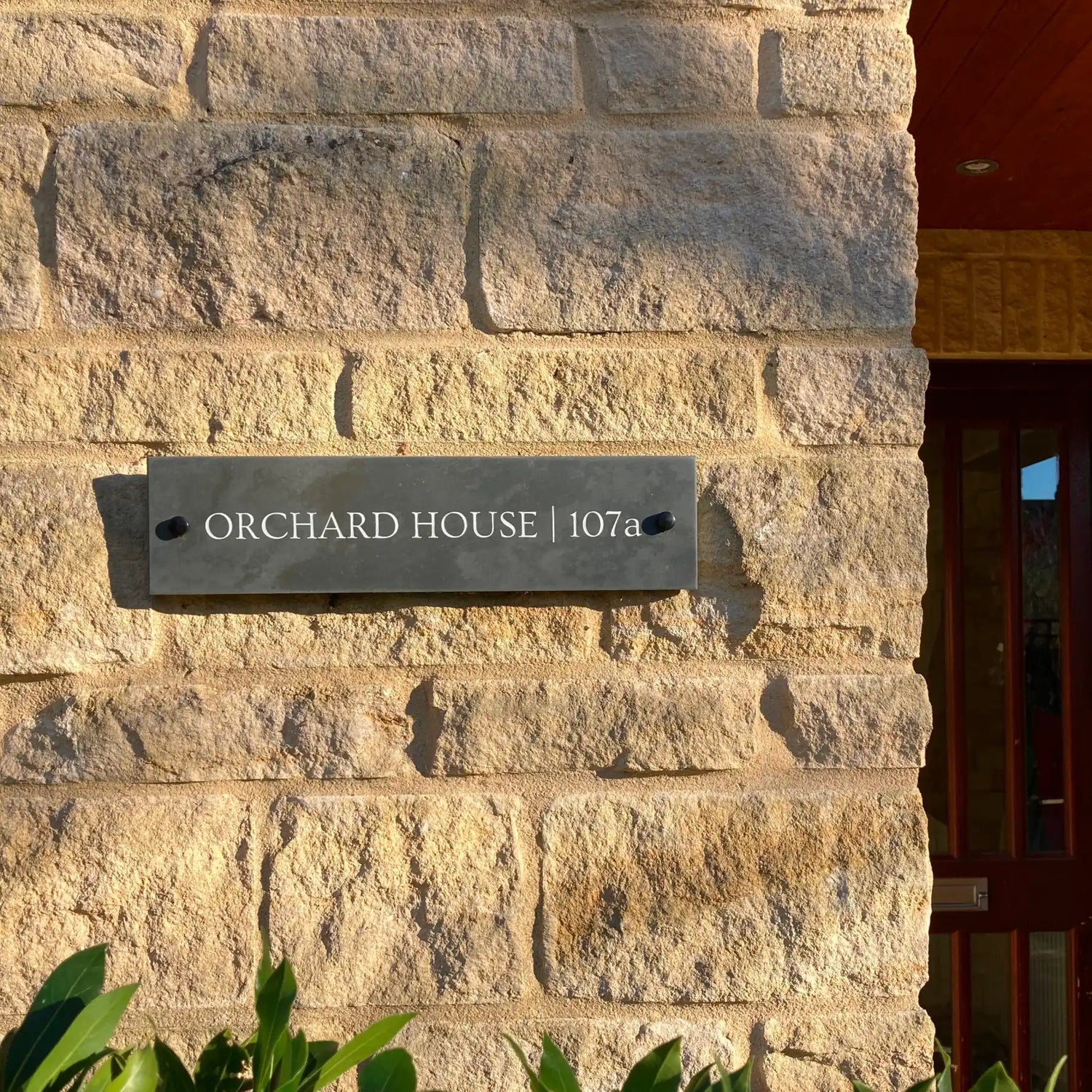 House sign on a stone wall with 'Orchard House | 107a' text