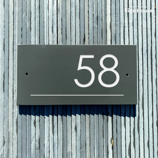 This image shows a rectangular slate sign mounted on a vertically striped, weathered slate surface. The sign prominently features the number "58" in large, white, modern sans-serif font, centered on the slate. Below the number, there is a thin white line spanning the width of the sign. There are two small holes on either side of the slate, suggesting where screws or nails would attach the sign to the wooden surface.
