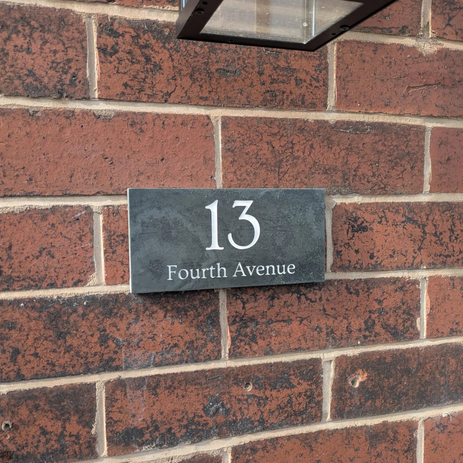 House number 13 on a slate plaque mounted on a brick wall.