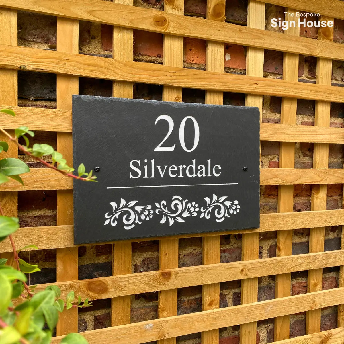 a welsh slate house sign with a house name, street number and floral design. Sign is positioned on a wooden trellis wall