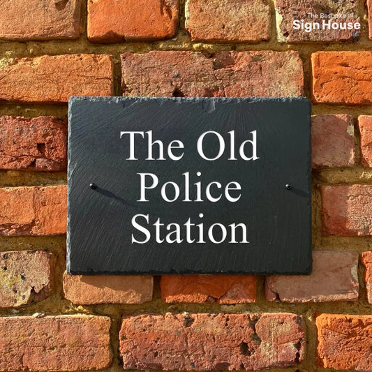 a black sign made using welsh slate. The sign is screwed into a red brick wall with the house name "The old police station" engraved onto it and painted white. The font is times new roman 