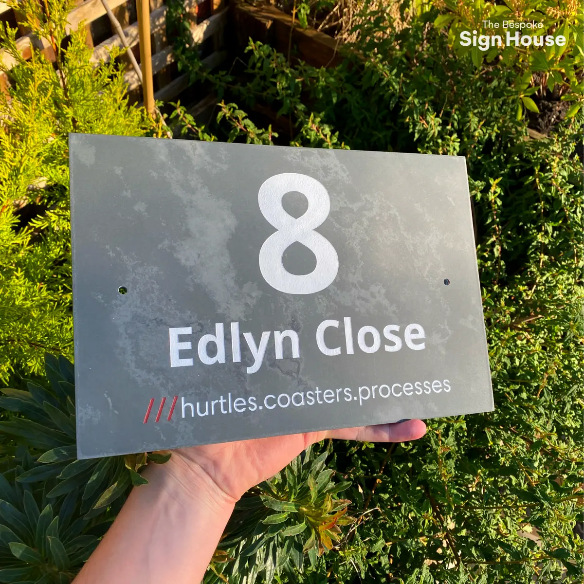 a grey slate sign with a customers house address engraved into it along with their what3words address. The sign reads 8 Edlyn Close ///hurtles.coasters.processess