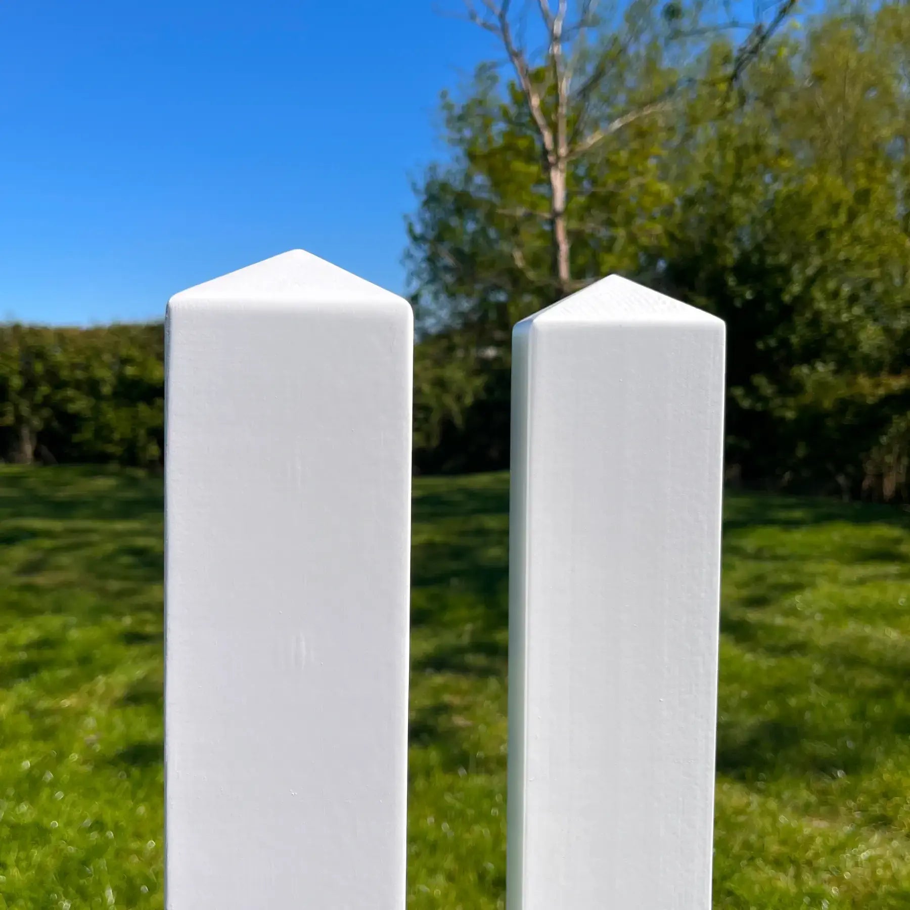 Two white cylindrical posts on a grassy field with trees in the background