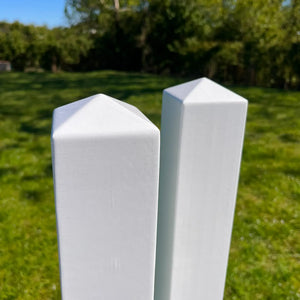 Two white fence posts on a grassy field with trees in the background