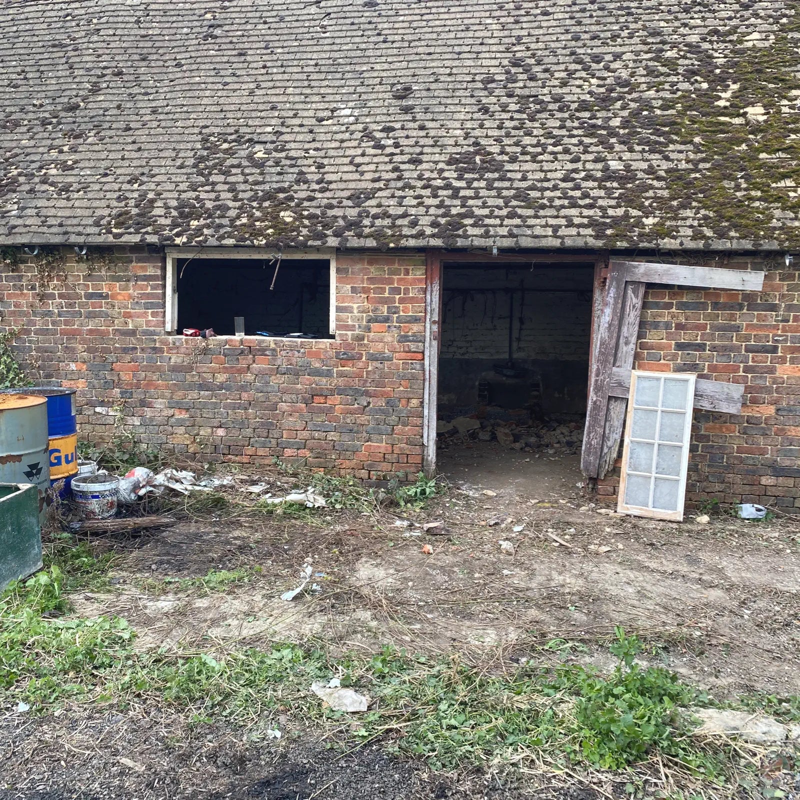 Old brick building with a slanted roof, showing signs of wear and neglect.