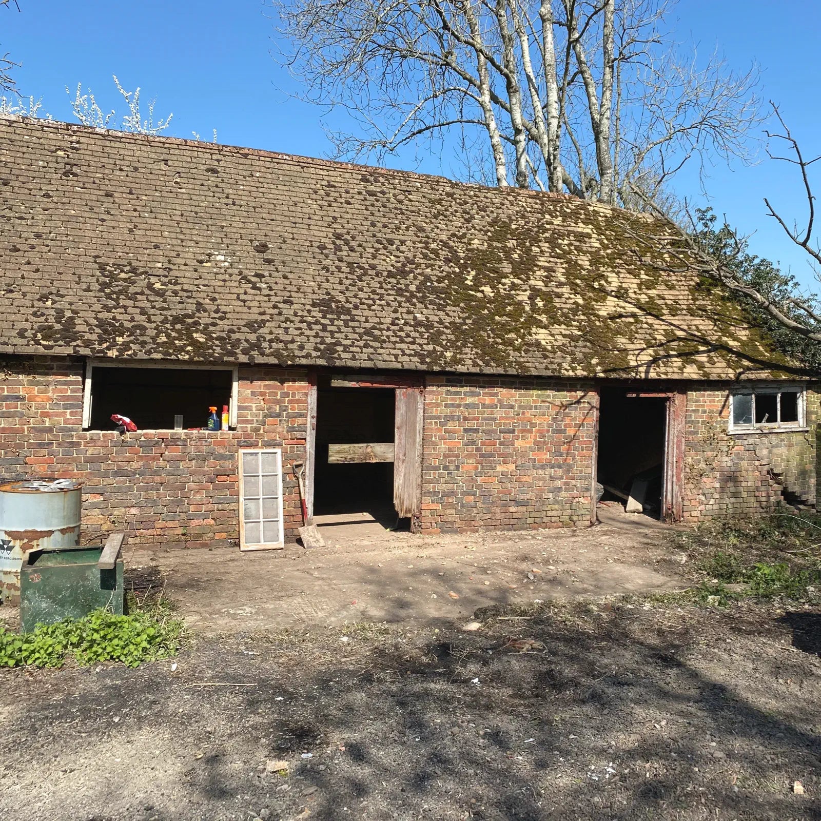 Brick building with a sloped roof, windows, and open doors on a sunny day.